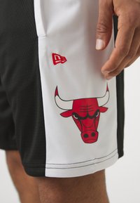 Svart-og-hvitt basketballshorts med et rødt brodert Bulls-logo på siden, med mesh-struktur og kontrasterende detaljer.