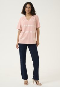 Lichtroze V-hals top met korte mouwen, met horizontale metallic strepen. Gepaard met donkerblauwe rechttoe-rechtaan jeans en beige sandalen.