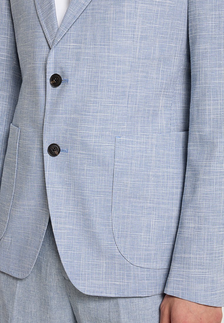 Blazer a quadri blu chiaro con due bottoni scuri indossato sopra pantaloni blu chiaro coordinati e una camicia bianca.
