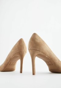 Beige semišové lodičky na vysokém podpatku s špičatou špičkou a štíhlým jehlovým podpatkem. Mají texturovanou podrážku pro lepší přilnavost. Minimalistický design.