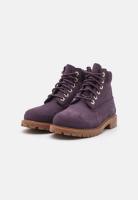 Botas de tobillo de ante púrpura con suelas de goma marrón, ojales de metal y cordones. Presentan un collar acolchado y una superficie texturizada para mayor agarre.