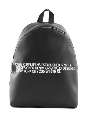 Sac à dos noir Calvin Klein avec texte blanc indiquant la création de la marque en 1978 et l'adresse à New York sur la poche avant.