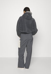 Mörkgrå kort fleecehoodie med foder i huvan, kombinerad med löst sittande grå byxor som har ett krämfärgat ficklock.