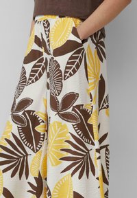 Pantalons évasés en blanc, ornés d'un imprimé audacieux de feuilles jaunes et marron. Fabriqués en tissu texturé avec poches.