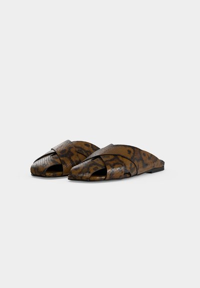 Paire de sandales plates à enfiler avec motif peau de serpent marron et noir, brides croisées et orteils ouverts sur un fond uni.