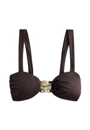Kobieta w ciemnym bikini idzie wzdłuż słonecznej plaży, na tle woda odbijająca światło, patrzy w dół.