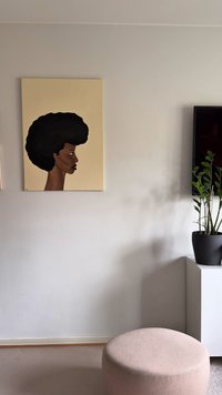 Didelio, tekstūruoto juodo afro šoninis profilis vaizduojamas drobės kūrinyje, o fono spalva yra smėlio. 
