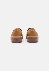 Zapatos de cuero marrón con un acabado texturizado, que presentan una suela gruesa y estriada en un color contrastante y un pequeño logo de TOMS en el talón.