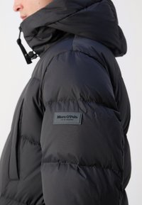 Schwarze Daunenjacke mit gesteppter Optik, ausgestattet mit einer Kapuze und einem Logopatch am linken Ärmel. Glatte, glänzende Textur.