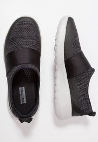 Baskets noires de sport à enfiler, avec une tige texturée, une large sangle en satin et une semelle en caoutchouc blanc dotée de crampons arrondis pour une meilleure adhérence.