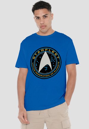 Blaues Baumwoll-T-Shirt mit einem runden Grafikdesign, das ein silbernes Starfleet-Logo und den Text "VEREINTE VÖLKER DER PLANETEN" in Gelb zeigt.