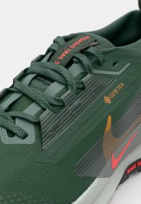 Green Nike shoes featuring Gore-Tex material, textured upper, and a patterned side panel. Bold orange and pink accents near the logo.