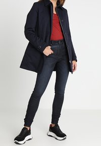 Námořnický modrý kabát s límcem a knoflíky, nošený přes červený top. Vytvořený s tmavými džíny a černými teniskami s bílou podrážkou.