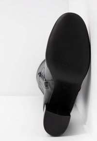 Botín negro de cuero hasta el tobillo con tacón cuadrado, que presenta una textura suave y sutiles detalles de costura, mostrado desde un ángulo trasero. Talla 37.