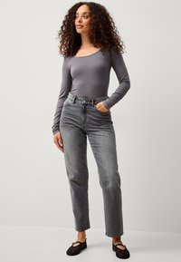 Graues Langarmoberteil mit rundem Ausschnitt, kombiniert mit hochgeschnittenen, geraden grauen Jeans und schwarzen Mary-Jane-Pumps.