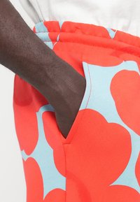 Κόκκινο παντελόνι φόρμας με μεγάλο ανοιχτό μπλε αφηρημένο σχέδιο. Διαθέτει απαλή υφή και πλαϊνή τσέπη, με ελαστική μέση.