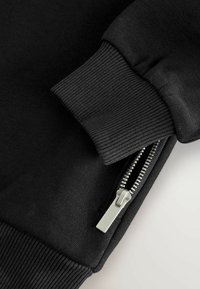 Black sweatshirt with ribbed cuffs and a side zipper. Features a smooth texture and silver zipper hardware for functionality.