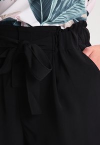 Mustat kangashousut, joissa on vyötärönauha, sivutaskut ja sileä pinta. Suunnittelussa on kerrostettu vyötärölinja.