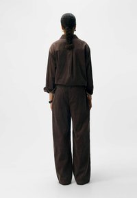 Brun corduroy skjorte og matchende bukser. Outfittet har en afslappet pasform, vide ben og lange ærmer med oprevne manchetter.