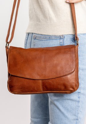 Braune Leder-Crossbody-Tasche mit Klappenverschluss, ausgestattet mit einer glatten Textur und einem schlichten Design. Verstellbarer Tragegurt und kompakte Form.