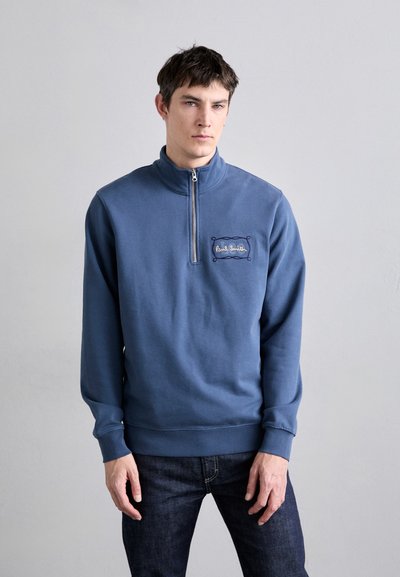 Blauwe sweatshirt met een hoge kraag, halve rits en geborduurd logo in een decoratief kader. Beschikt over lange mouwen en ribgebreide manchetten.