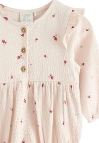 Vaaleanpunainen mekko, jossa on pieniä punaisia kukkakuosisia, pyöreä kaula-aukko, kolme puusta valmistettua nappia ja rypytetty pinta vyötäröllä.