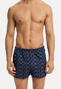 Námořnické modré plavky s vzorem, volnějšího střihu, elastickým pasem a dekoračním knoflíkem vpředu; mají geometrický design.