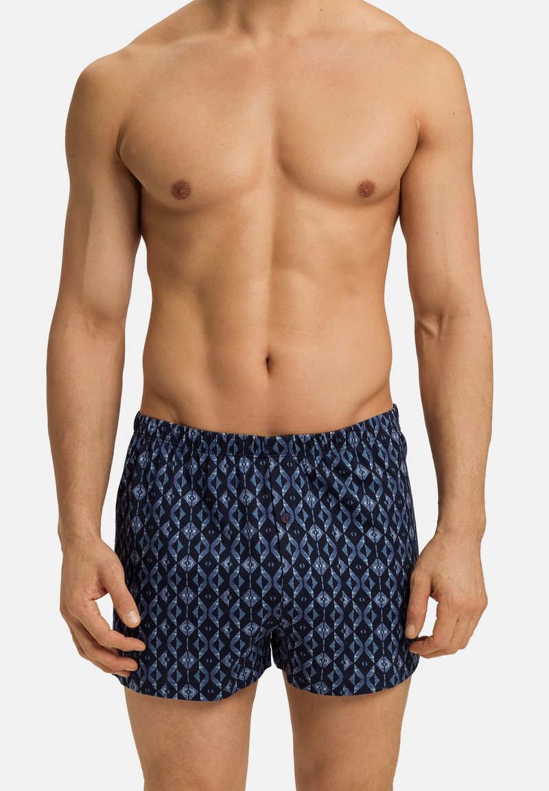 Námořnické modré plavky s vzorem, volnějšího střihu, elastickým pasem a dekoračním knoflíkem vpředu; mají geometrický design.
