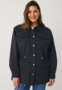 Giacca blu scuro con chiusura a bottoni, due tasche sul petto, cordini regolabili in vita e vestibilità comoda.