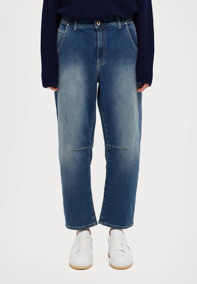 Jeans in denim blu chiaro con una vestibilità rilassata, caratterizzati da cuciture visibili e un design a gamba dritta. Indossati con sneakers bianche.