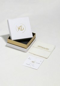 Vit och guld smyckeslåda, öppen för att avslöja en svart interiör. Innehåller en vit påse med texten "HAZE & GLORY" och ett varumärkesmärke.