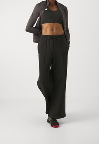 Svart atletisk ensemble med en kortärmad sport-bh och löst sittande sweatpants. Outfiten inkluderar en jacka med dragkedja och mönstrade sneakers.