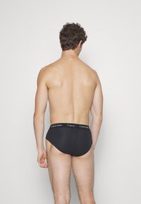 Schwarze Baumwollunterhose mit weichem Bund, auf dem das "Calvin Klein"-Logo zu sehen ist. Sie hat einen klassischen Schnitt und eine glatte Textur und ist von hinten betrachtet.