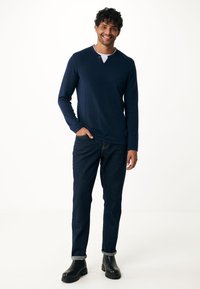 Maglietta henley a maniche lunghe blu navy con colletto a bottoni, abbinata a jeans in denim scuro e stivaletti neri alla caviglia, con polsini arrotolati.