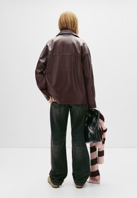 Bordo umjetni kožni overshirt s ovratnikom, opuštenog kroja, s rukavima na manžetama, u kombinaciji s tamnim trapericama i crnom torbom, drži prugasti pulover.