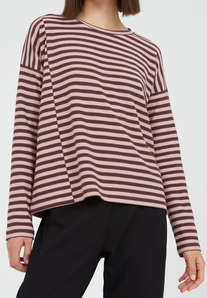Woman wearing a long-sleeve pink and brown horizontal striped shirt paired with black pants, shown from neck to hips.