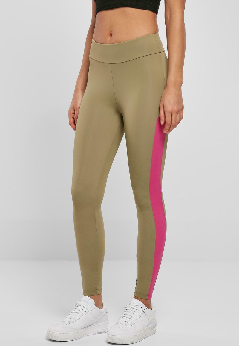 Olivengrønne tights med en lyserød sidestripe; strækbart materiale, høj talje, tætsiddende design, kombineret med hvide sneakers.