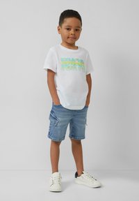 Witte katoenen T-shirt met kleurraf "TOKYO" grafiek, gecombineerd met denimshorts met zijzakken, en witte sneakers met zwarte accenten.