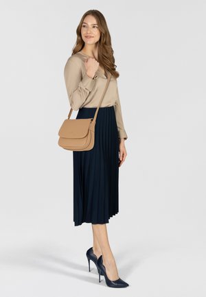 Schoudertas van tan leer met een gladde textuur en een klepsluiting, gedragen door een model met een geplooide marineblauwe rok en bijpassende hakken.
