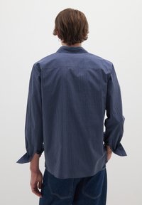 Camicia a quadri blu navy con colletto strutturato, maniche lunghe e dettagli con bottoni. Presenta una vestibilità rilassata e una trama di tessuto traspirante.