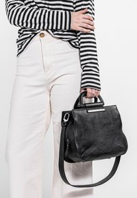 Musta nahkakäsilaukku, jossa on strukturoitu muoto, lyhyet kahvat ja irrotettava olkahihna. Varustettu hopeanvärisillä yksityiskohdilla.