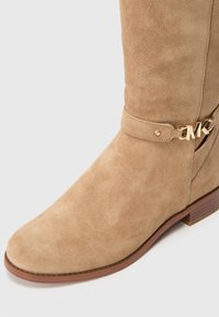 Tan suede mid-calf boot with wooden sole and gold MK logo detail on side strap.