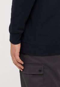 Navy blue sweatshirt made of cotton blend, featuring ribbed cuffs and hem. Dark gray cargo pants with a flap pocket and black snap button.