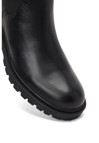 Bottine en cuir noir avec une surface lisse, une pointe arrondie et une semelle en caoutchouc robuste avec des crampons profonds. Panneaux élastiques latéraux pour un enfilage facile.