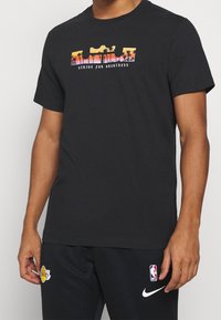 Camiseta de algodón negra con un gráfico colorido de palmeras y el texto "LUCHA POR LA GRANDEZA" en el pecho. Manga corta, cuello redondo.