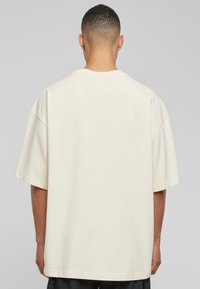 Løstsittende T-skjorte med korte ermer i beige bomull, med rund hals og rett nederkant. Ingen synlige mønstre eller detaljer.