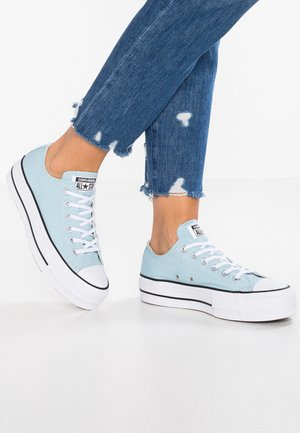Baskets à plateforme Converse bleu clair avec lacets blancs portées avec un jean bleu à ourlet effiloché, présentées sur un fond blanc.