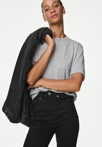 Grå kortärmad t-shirt tillsammans med högmidjade svarta jeans. En svart denimjacka hänger över ena axeln. Släta tyger.