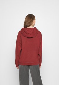Felpa bordeaux con grande cappuccio regolabile, vestibilità comoda, polsini e orlo a coste; il tessuto sembra morbido e leggermente strutturato.