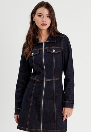 Robe en denim foncé avec manches longues, fermeture éclair sur le devant et deux poches poitrine, présentant des coutures contrastantes orange et une silhouette ajustée.